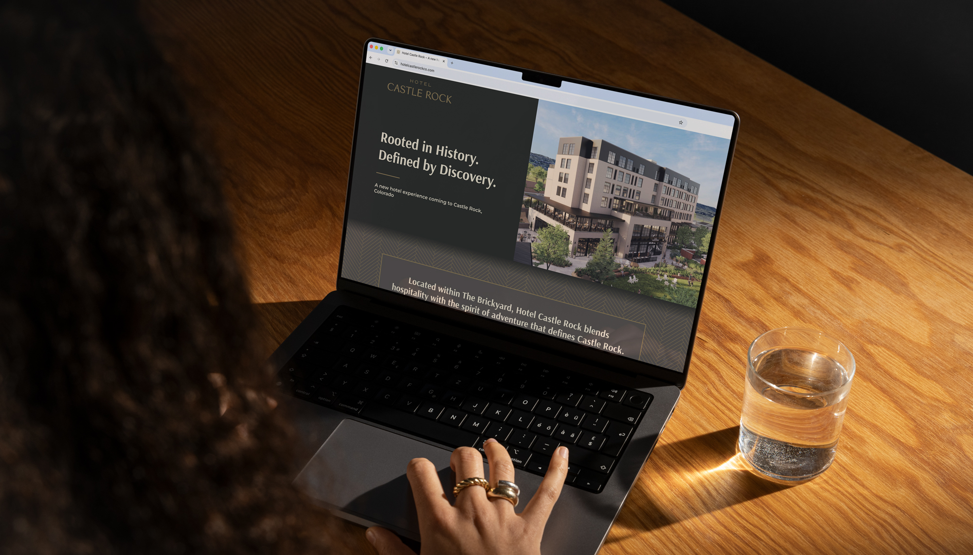 Woman using her laptop to view the Hotel Castle Rock website at a desk with a glass of water